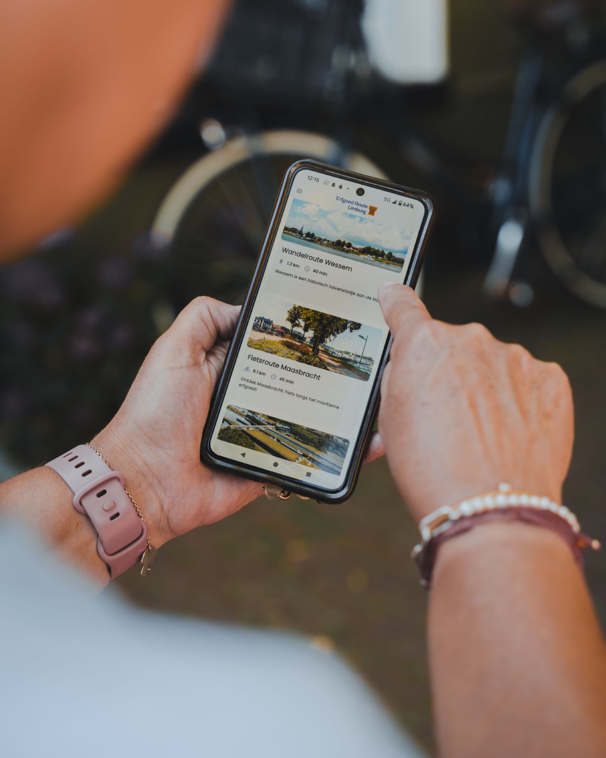 A person holds a smartphone showing the Erfgoed Route Limburg app, used to explore a route of the legend of Saint George and the Dragon