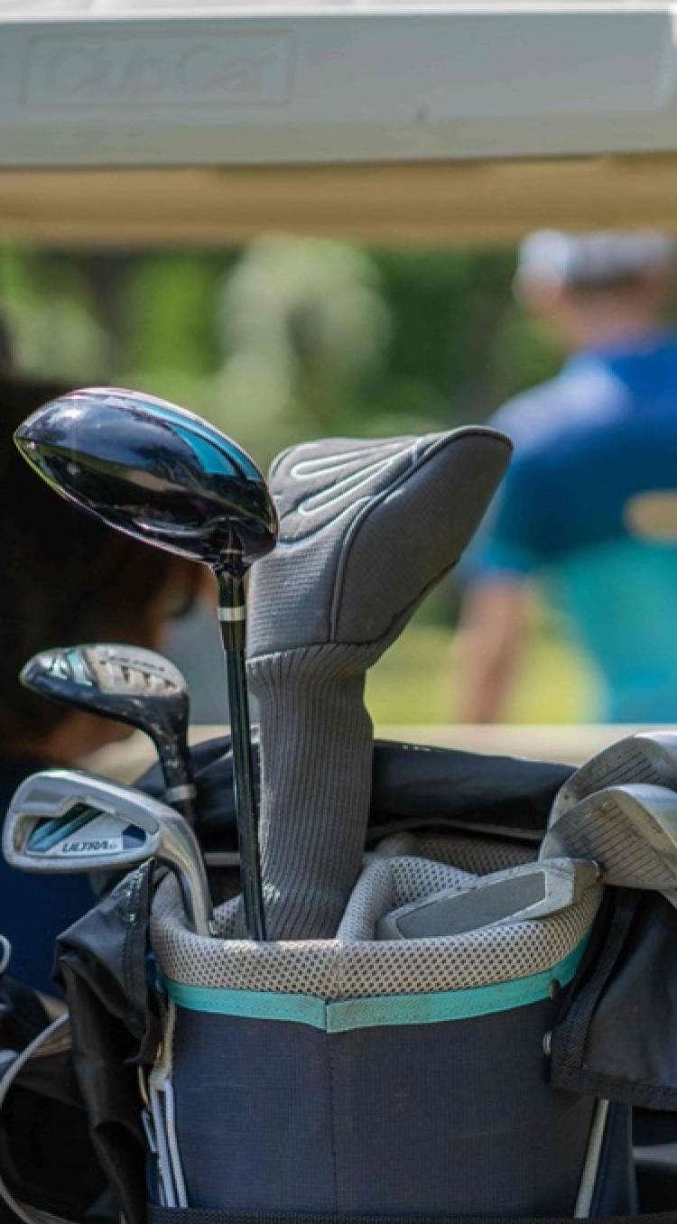 Golfclubs in een golftas op een golfkar, met golfers op de achtergrond in een groene omgeving.