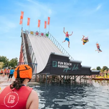 Superslide bij Fun Beach Event & Leisurepark: bezoekers maken spectaculaire sprongen vanaf de 14 meter hoge glijbaan het water in.